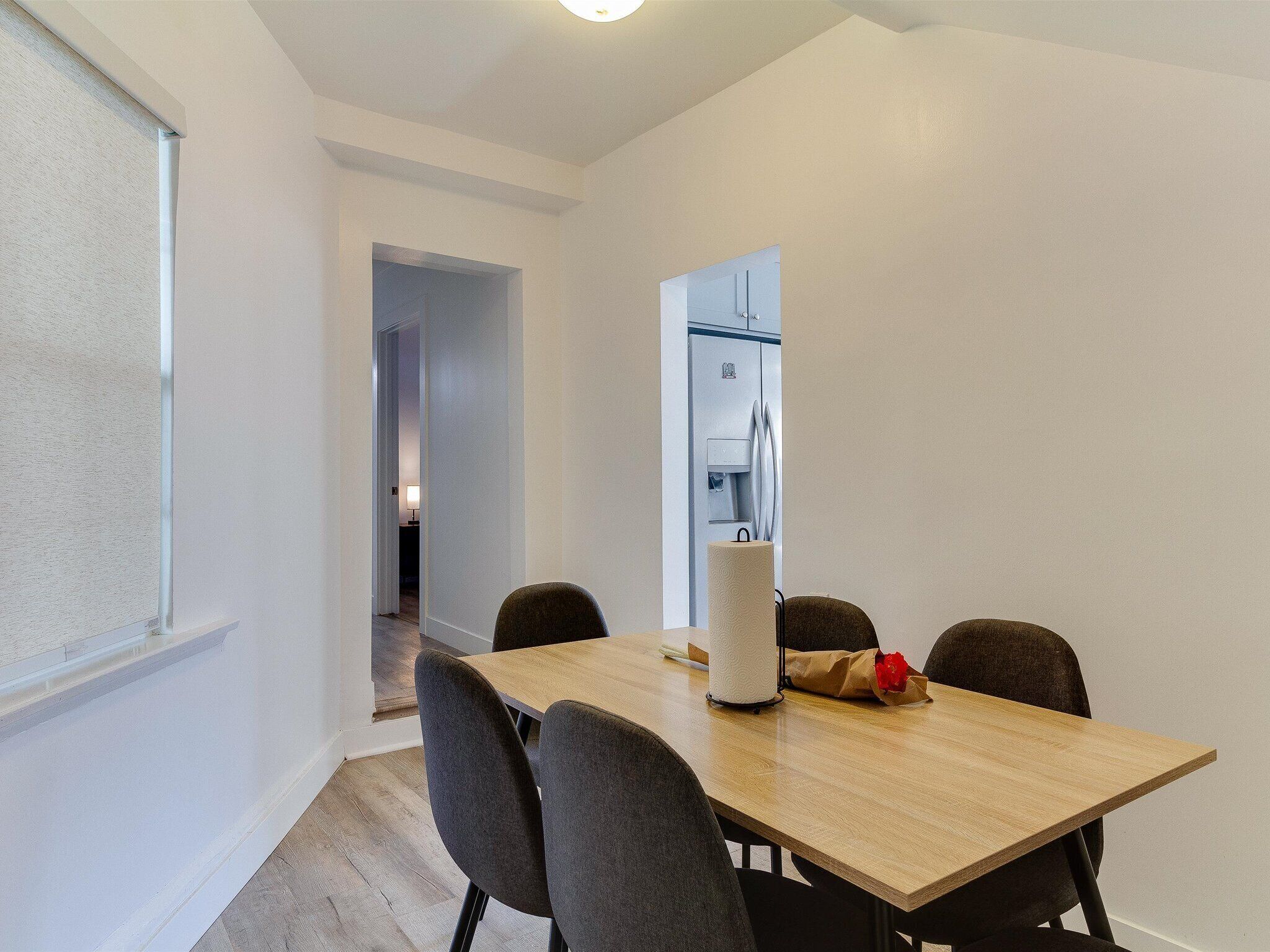 Un coin repas avec une table en bois, quatre chaises, un distributeur de serviettes en papier blanc et un bouquet de fleurs rouges.