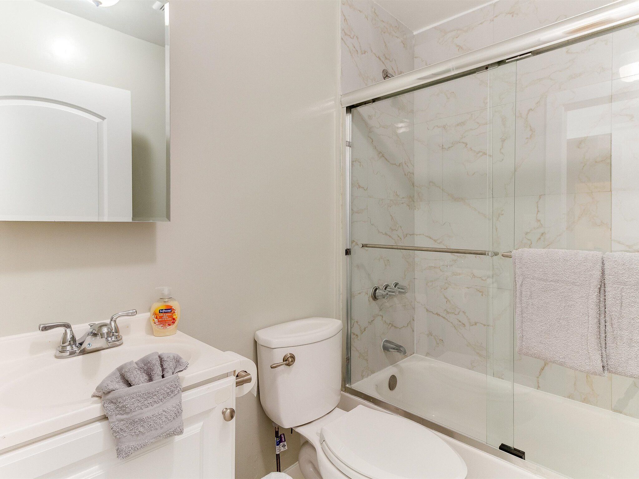 Un baño moderno con ducha de vidrio, un lavamanos blanco con espejo y un inodoro.