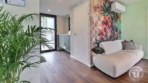 A modern living room with a sofa, a large floral tapestry, and a potted plant. - My Cottage in Canada (GOSNE)