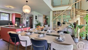 A modern kitchen with a central island, a dining area with chairs and a table set for four, and a staircase leading to an upper level. - My Cottage in Canada (GOSNE)