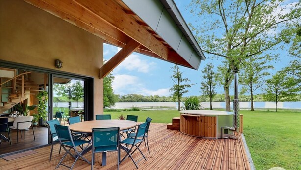 A wooden deck with a round table and chairs, a hot tub, and a view of a lake. - My Cottage in Canada (GOSNE)