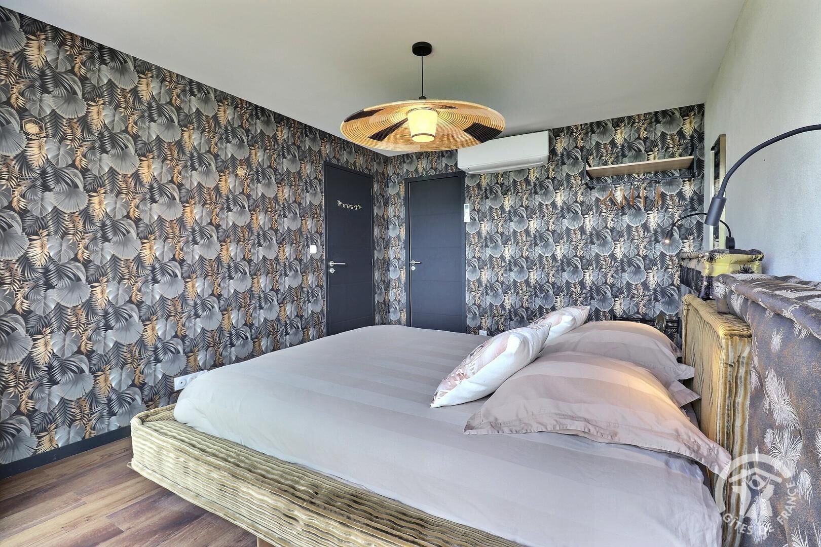 A bedroom with a bed, a woven basket, a wall-mounted air conditioner, and a door with a sign.