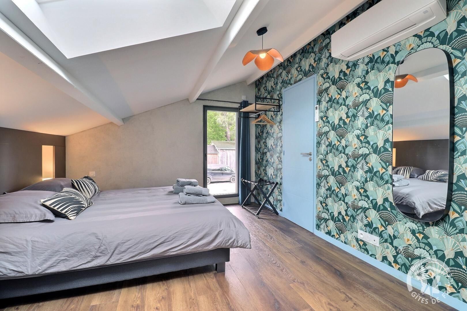 Une chambre à coucher avec un lit, un grand miroir et une fenêtre donnant sur l’extérieur.
