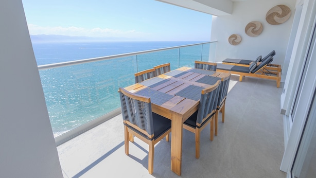 A balcony with a wooden table and chairs, overlooking a clear blue sea.
