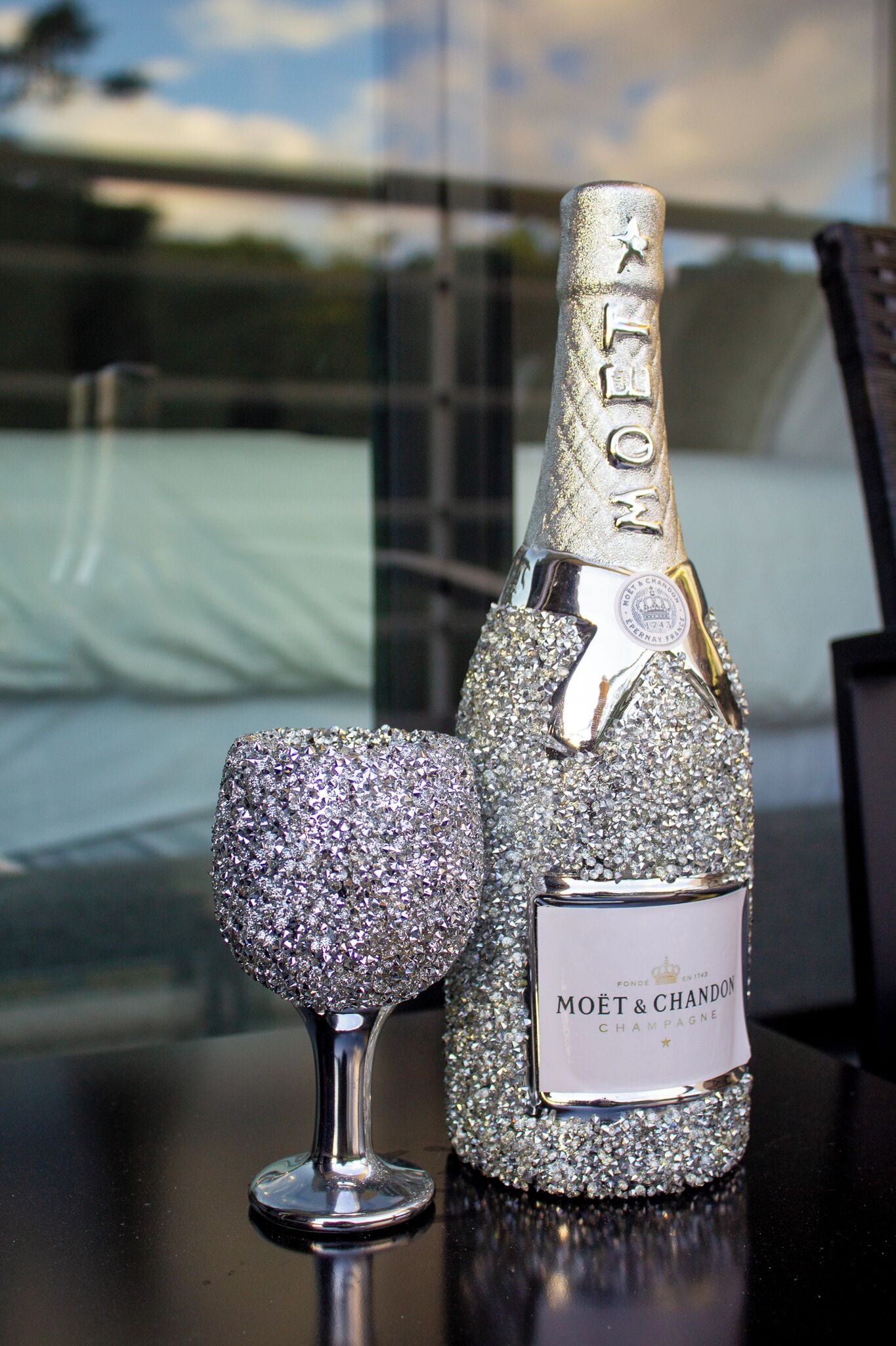 Een fles Moët & Chandon champagne met een glinsterend, sierlijk ontwerp, geplaatst naast een vergelijkbaar versierd glas op een reflecterend oppervlak.