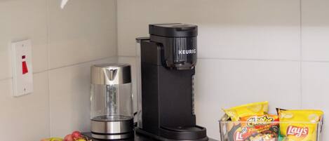 A kitchen with a coffee maker, kettle, microwave, and a bowl of fruit.