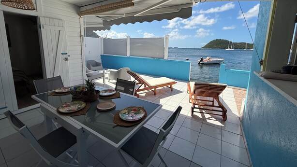Una terrazza esterna con tavolo apparecchiato per mangiare, poltrone relax e vista sul mare.