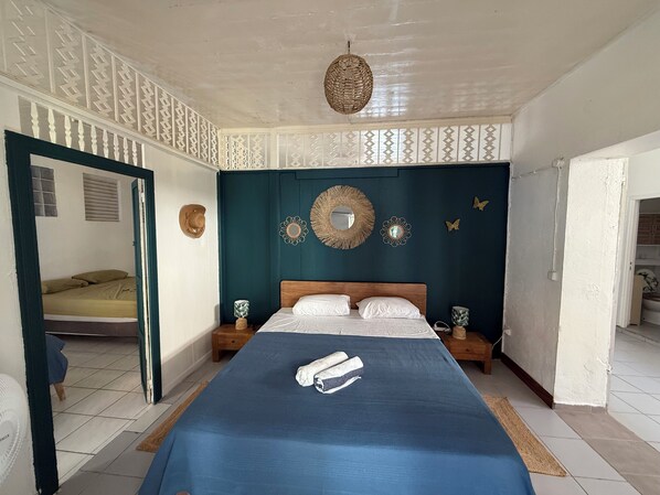 Une chambre à coucher avec un grand lit, une tête de lit en bois, des miroirs décoratifs sur les murs et un luminaire suspendu au plafond, fait d’un matériau tressé.