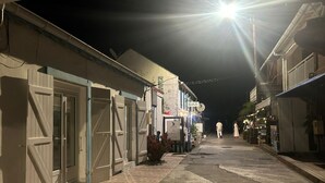 Una stretta via fiancheggiata da edifici, alcuni con persiane chiuse, e qualche insegna che indica un bar.
