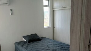 Ein kleines, modernes Schlafzimmer mit einem Einzelbett, einem Fenster und einem Kleiderschrank.