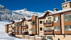 A multi-story hotel with balconies, set against a snowy mountain backdrop.