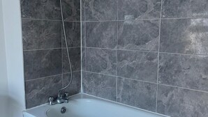 Un bagno con vasca, doccia e parete rivestita di piastrelle.