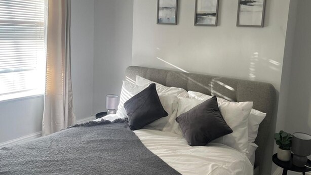 Un letto rifatto con cura, con biancheria bianca e grigia, una testiera grigia e tre quadri appesi al muro.