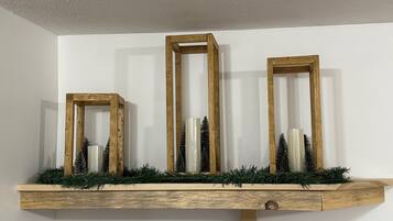 Un estante de madera con tres marcos rectangulares que contienen pequeños árboles de Navidad y velas.