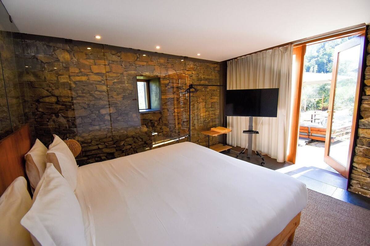 Een slaapkamer met een stenen muur, een bed, een televisie en een schuifdeur naar een buitenruimte.
