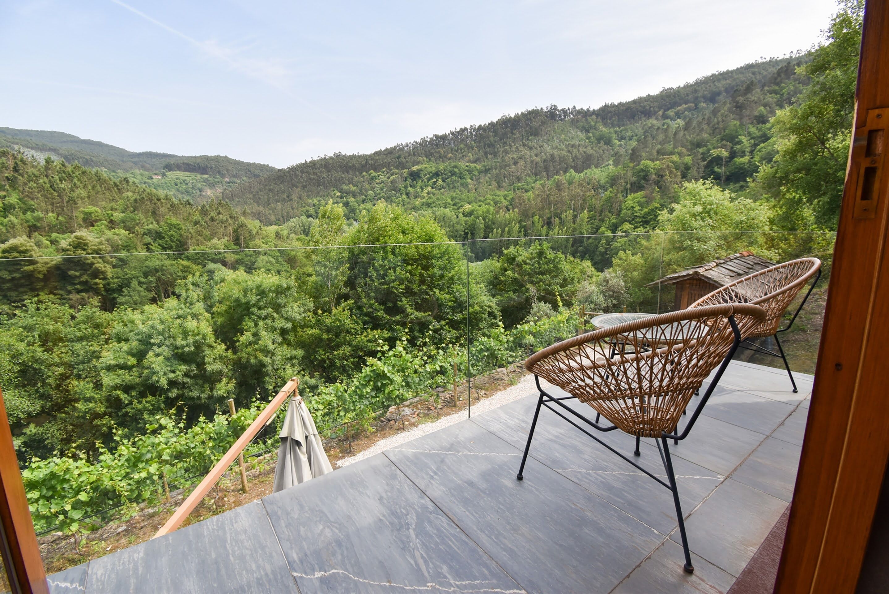 A balcony with wicker chairs overlooking a forested valley.