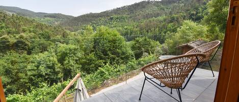 A balcony with wicker chairs overlooking a forested valley.