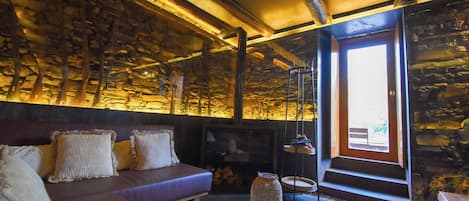 Una sala de estar acogedora con pared de piedra, un sofá, un televisor y un ventanal grande.