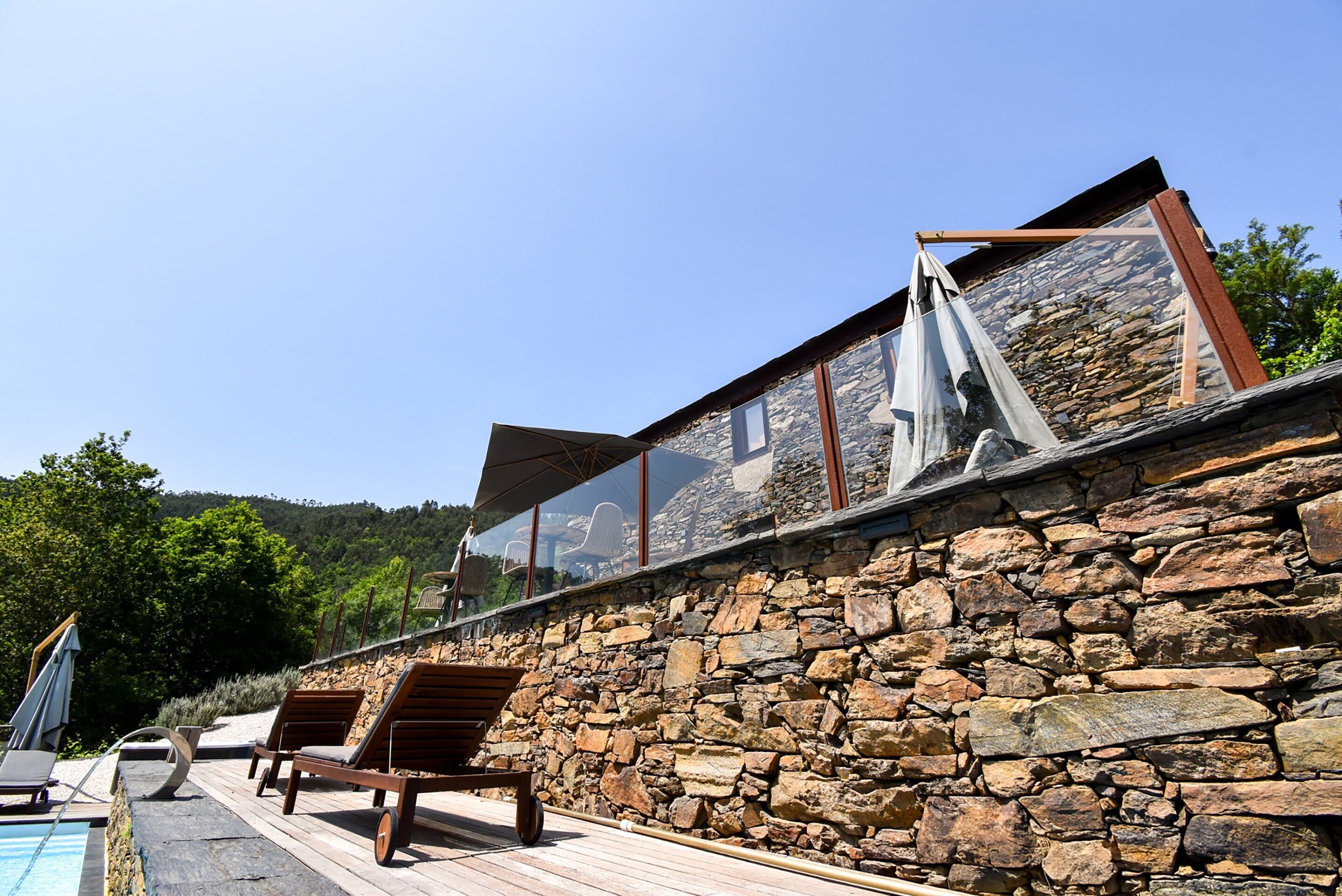 A stone wall with a wooden deck and lounge chairs.