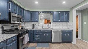 A modern kitchen with dark blue cabinets, a stainless steel microwave, a gas stove, and a dishwasher. - Yinzer On The Mount - 5 Min. To Downtown  (Pittsburgh)