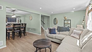 A modern living room with a sofa, a dining table with chairs, a small round table, and a staircase leading to another level. - Yinzer On The Mount - 5 Min. To Downtown  (Pittsburgh)