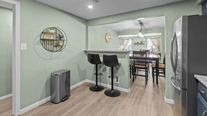 A kitchen with a bar area, two stools, a refrigerator, and a trash can. - Yinzer On The Mount - 5 Min. To Downtown  (Pittsburgh)