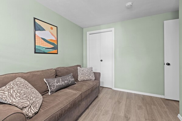 A living room with a brown sofa, patterned cushions, a framed abstract painting, and a white door. - Yinzer On The Mount - 5 Min. To Downtown (Pittsburgh)