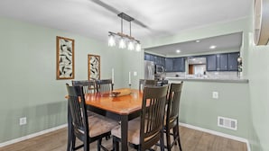 A dining area with a wooden table and chairs, a chandelier, and a kitchen in the background. - Yinzer On The Mount - 5 Min. To Downtown  (Pittsburgh)