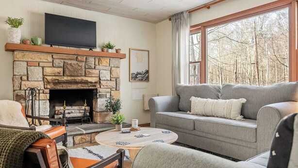 Ein gemütliches Wohnzimmer mit Kamin aus Stein, einem grauen Sofa und einem flachbildfernseher an der Wand.