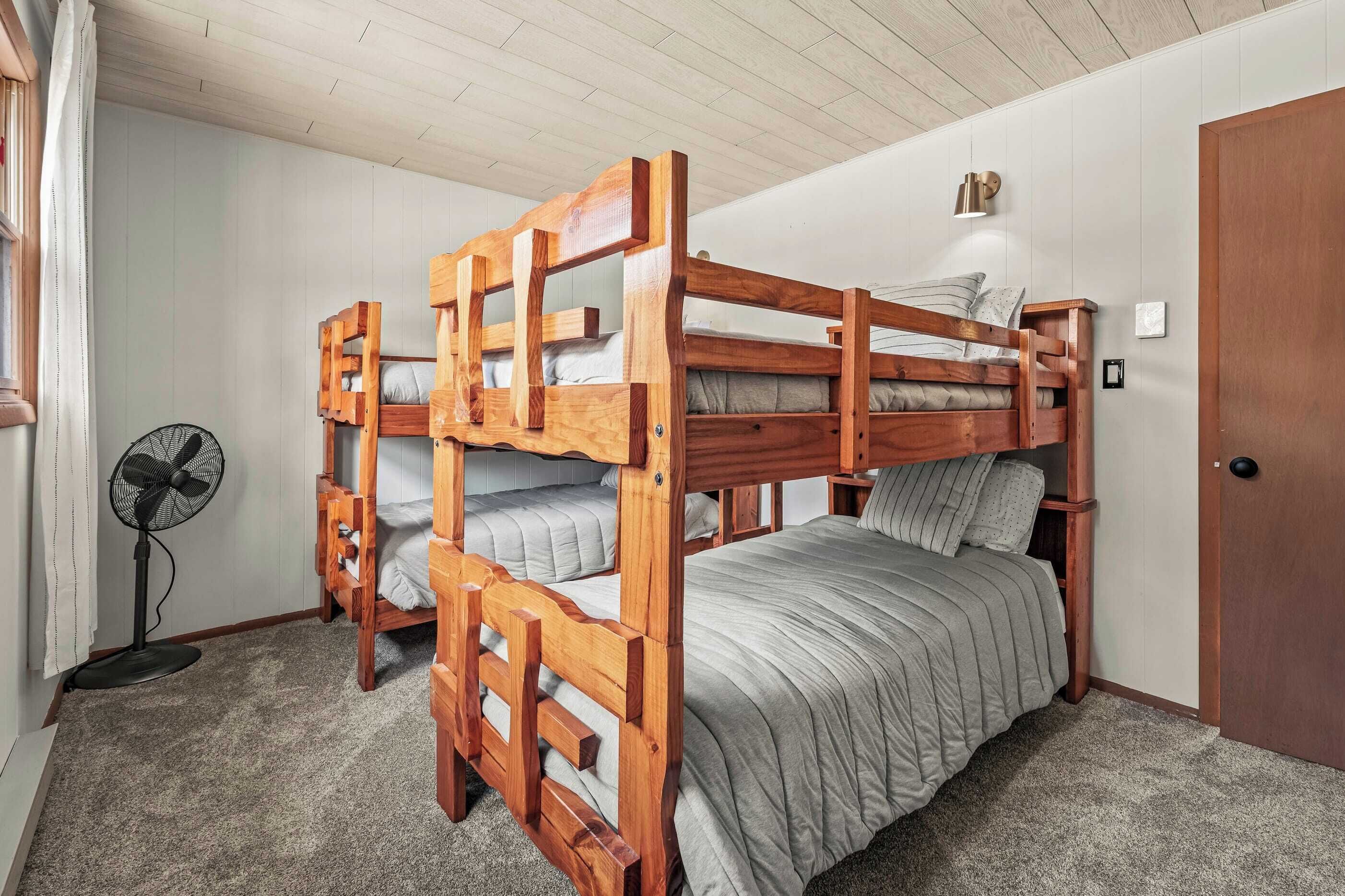 Een slaapkamer met een stapelbed, houten hoofdbord, een ventilator en een deur.