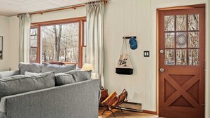 Ein gemütlicher Wohnraum mit einem grauen Sofa, einer Holztür mit Glasscheiben und Blick auf Bäume durch das Fenster.