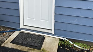 Une porte d’entrée blanche, surmontée d’une petite fenêtre, dans une maison bleue dont les murs sont recouverts de bardage.
