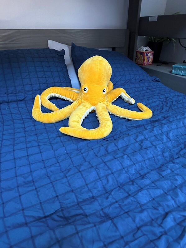 A bed with a blue quilt and a plush octopus toy on it.