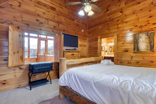 A wooden cabin room with a bed, a television, and a suitcase on a stand. - Anne's Place by Avantstay Cozy Cabin With Hot Tub, Games, Near Dollywood Attractions (Sevierville)