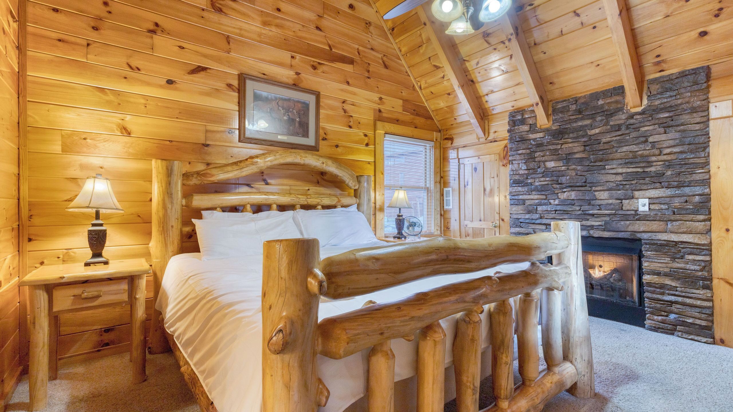 Une chambre à coucher dans un chalet en rondins, avec un lit, une table de chevet, une lampe, une cheminée et un tableau encadré au mur.