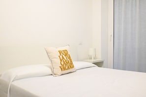 Hotellihuone, jossa on sänky, tekstillä varustettu tyyny, yöpöytä ja ikkuna, jossa on verhot.