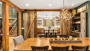 Un coin repas rustique avec une table et des chaises en bois, un lustre et une cuisine en arrière-plan.