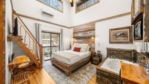 Une chambre avec un grand lit, une tête de lit en bois, une banquette intégrée, une fenêtre et une vue sur un paysage enneigé.