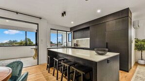 A modern kitchen with a large island, bar stools, and a view of the outdoors. - Luxury accommodation close to the beach and main street. (Kingston SE)