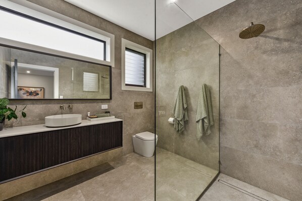 Un baño moderno con cabina de ducha de vidrio, un espejo grande y un mueble de tocador de madera oscura.