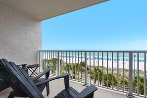 A balcony with a view of a beach, a table, and two chairs.