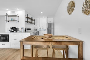 A modern kitchen with white cabinetry, a wooden dining table, and a stainless steel refrigerator.