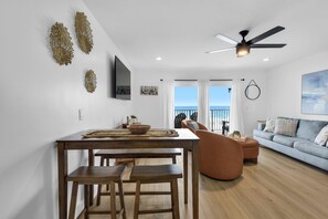 A modern living room with a dining area, a ceiling fan, and a view of the sea.