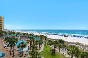 A beach resort with a swimming pool, palm trees, and a view of the ocean.