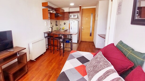 Um espaço compacto com cozinha americana, área de refeições e cama com colcha colorida.