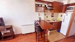 Uma cozinha compacta com uma mesa de madeira, banquetas, micro-ondas e geladeira.