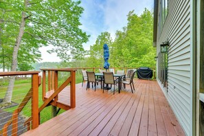 Eine Holzterrasse mit Tisch und Stühlen, einem überdachten Grill und Blick auf ein bewaldetes Gebiet.