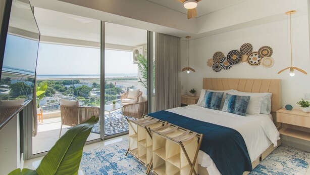Una habitación de hotel moderna con una cama grande, un balcón con vistas, un ventilador de techo y decoración mural.