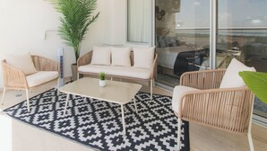 Un espacio de sala moderno con mobiliario de mimbre, una alfombra estampada y un gran ventanal con vistas.