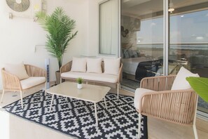 Un espace de vie moderne avec des meubles en osier, un tapis à motifs et une grande fenêtre offrant une vue dégagée.